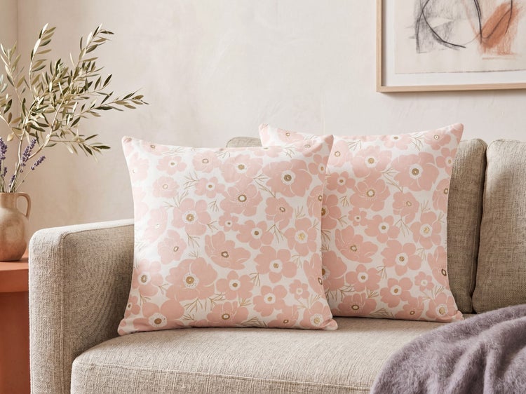 Zwei quadratische Dekokissen mit rosa Blumenmuster auf einem hellgrauen Sofa in einem hellen Wohnzimmer.