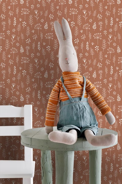 Dekoratives Stofftierhase sitzt auf einem kleinen Tisch vor einer floralen Tapete.