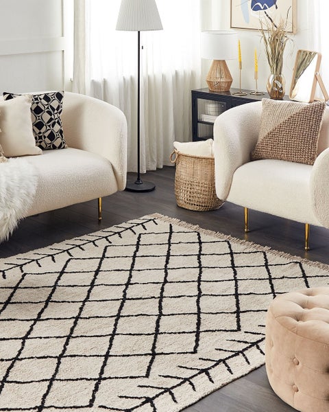 Hell gestaltetes Wohnzimmer mit geometrischem Teppich, Bouclé-Sesseln mit Goldbeinen, Stehlampe und geflochtenem Korb, modern und organisiert.