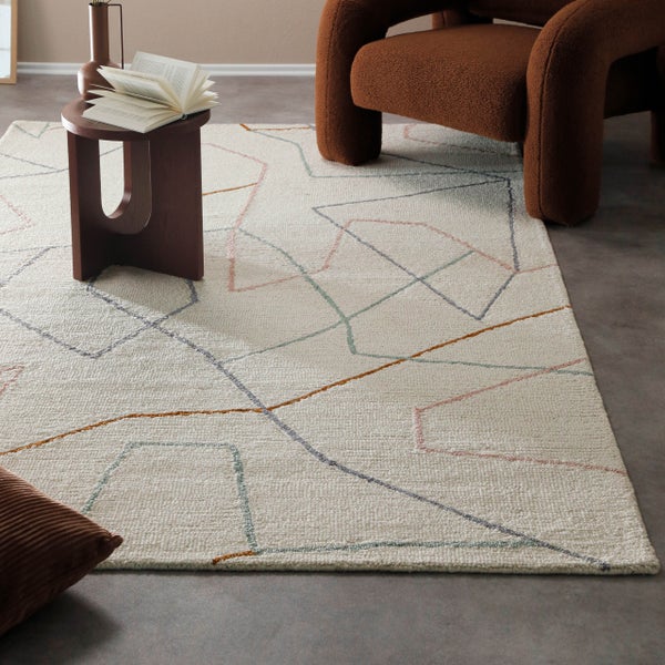 Moderner, heller Teppich mit geometrischem Linienmuster in einem Wohnzimmer mit braunem Sessel und Beistelltisch aus Holz.