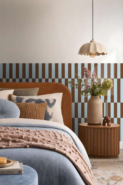 Modernes Schlafzimmer mit gestreifter Tapete, gepolstertem Bett, Holznachttisch und dekorativer Pendelleuchte.