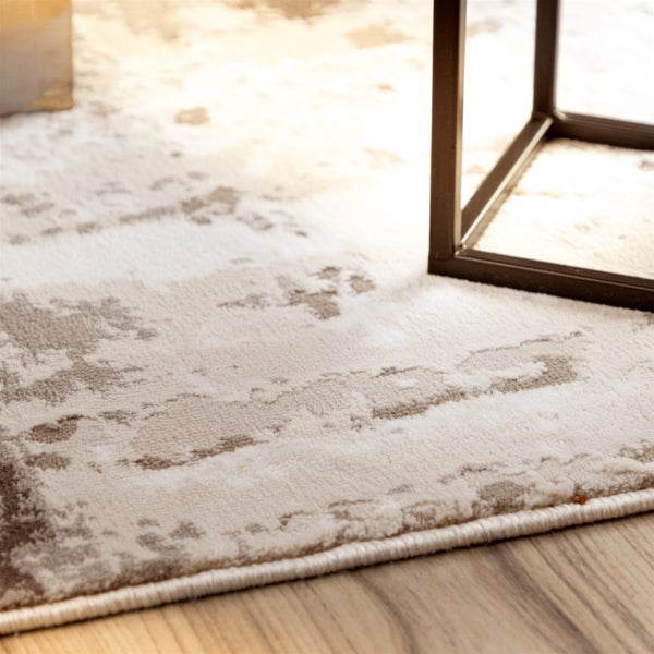 Nahaufnahme eines Teppichs mit abstraktem Muster und geketteltem Rand auf einem Holzboden unter einem Metallgestell.