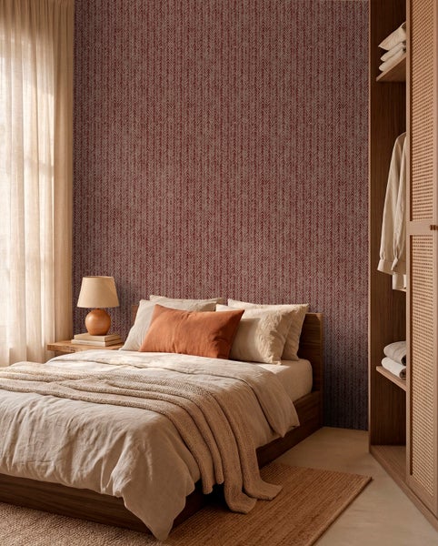Helles Schlafzimmer mit gemusterter Tapete, Holzbett mit heller Bettwäsche und einem Kleiderschrank aus Holz.