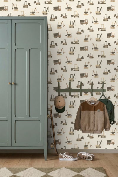 Hell gestaltetes Kinderzimmer mit einer gemusterten Tapete mit Baustellenfahrzeugen, einem grünen Holzschrank und einer Garderobe auf Holzfußboden.