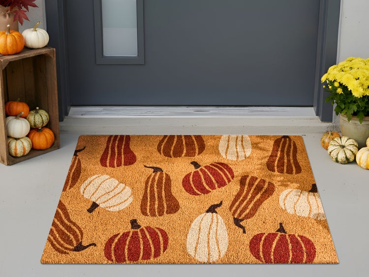 Fußmatte aus Kokosfasern mit Kürbis-Motiv vor einer Haustür mit herbstlicher Dekoration aus echten Kürbissen und Blumen.
