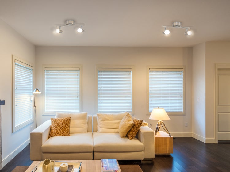Wohnzimmer mit Sofa, Fenstern mit Jalousien und Deckenleuchten