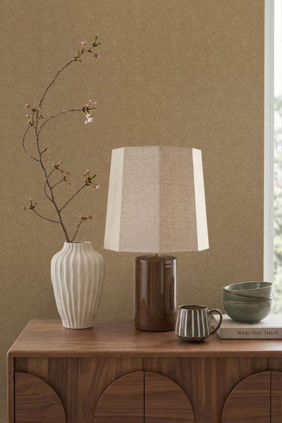Wohnraum mit brauner Tapete mit Fischgrätmuster, einem Holzkonsolentisch, einer Tischlampe mit Lampenschirm, einer Vase und Geschirr.