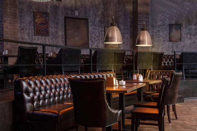 Innenaufnahme eines Restaurants mit Tischen, Stühlen, Ledersofas und Pendelleuchten