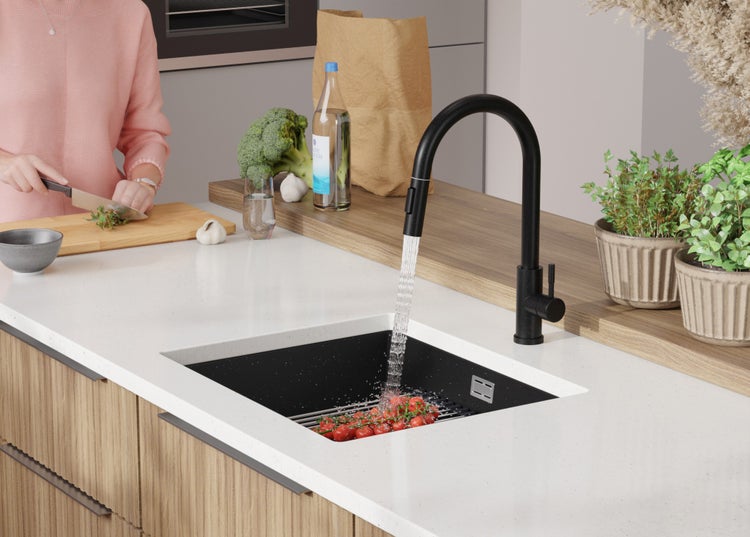 Küchenszene mit Spüle, Armatur und Person beim Gemüseschneiden