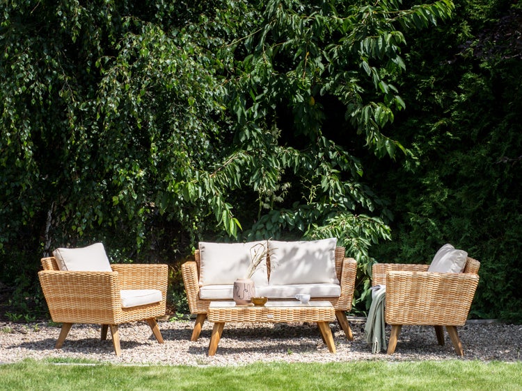 Gartenlounge-Set aus Rattan mit Tisch, Sofa und Sesseln vor grünem Hintergrund