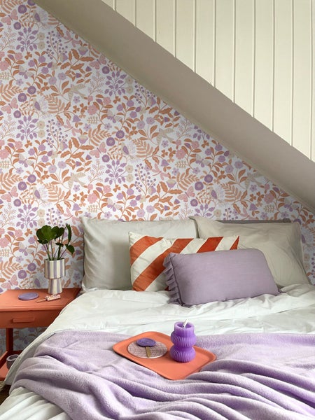 Helles Schlafzimmer mit floraler Tapete, einem Bett mit lilafarbenen Akzenten und einer Dachschräge mit Holzvertäfelung.