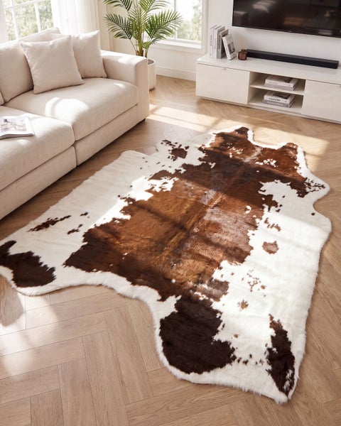 Wohnzimmer mit hellem Sofa und einem flauschigen Teppich im Kuhfell Design auf Fischgrät Parkettboden.