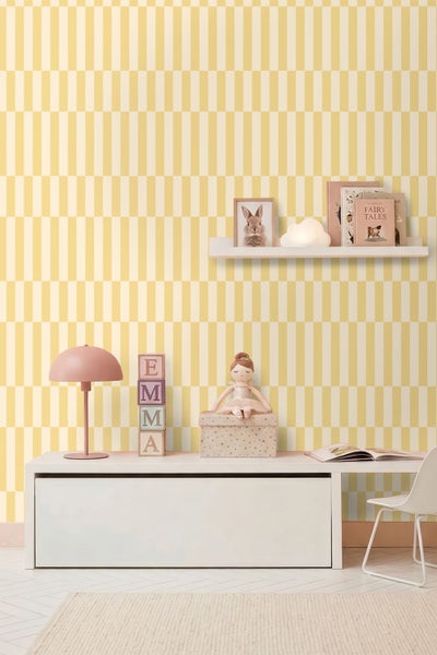 Kinderzimmer mit gelb-weiß gestreifter Tapete, weißer Sitztruhe, rosa Lampe und Wandregal mit Dekoration.