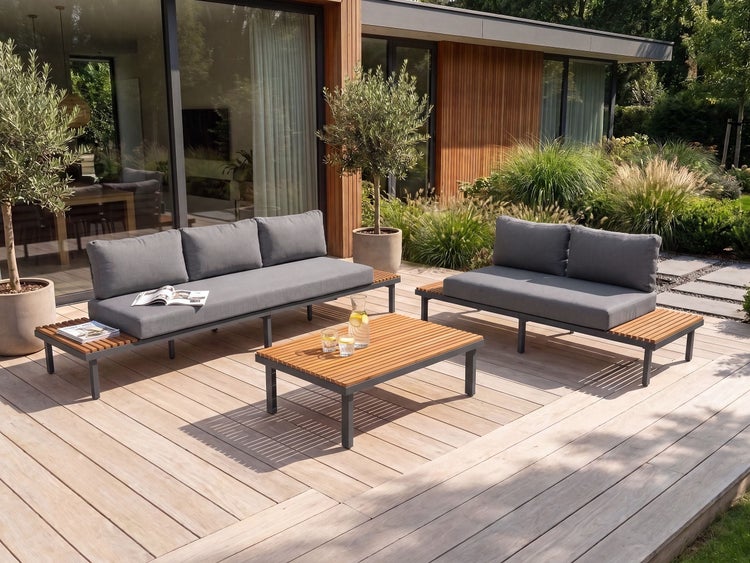 Moderne Loungegarnitur mit Holzrahmen und Polstern auf einer Holzterrasse vor einer modernen Villa mit grossen Fensterfronten.