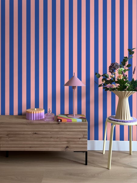 Einrichtung mit Kommode, Lampe, Dekorationen, Blumenstrauß und gestreifter Tapete