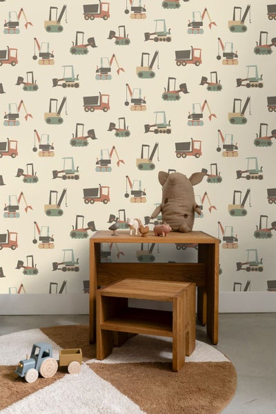 Tapete mit Baustellenfahrzeugen im Kinderzimmer mit Holzschreibtisch, Hocker und Spielzeugtraktor.