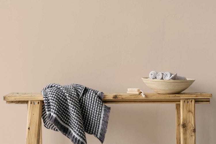 Organisierte Szene mit einer rustikalen Holzbank, einem gemusterten Baumwollhandtuch, einer Nagelbürste und einer Bambusschale mit Handtüchern.