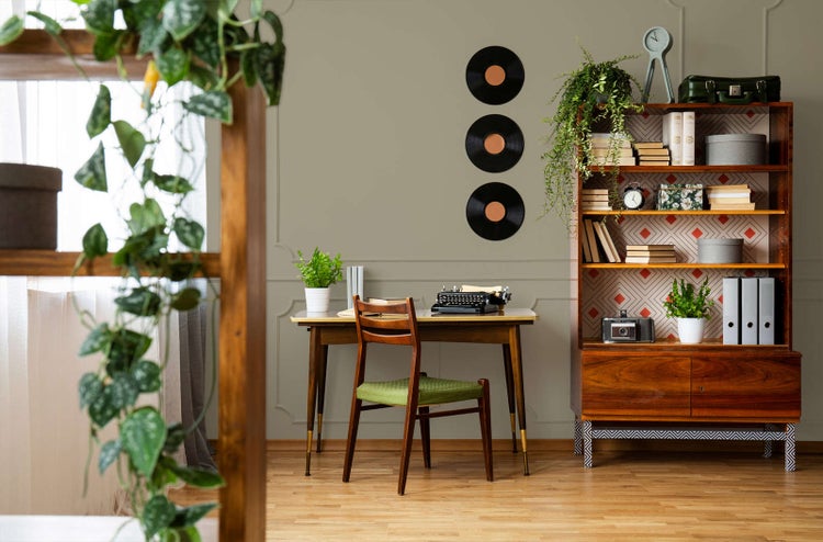 Eingerichtetes Zimmer im Vintage-Stil mit olivgrüner Wandfarbe und Zierleisten. Holztisch mit Schreibmaschine, Holzstuhl und großes Wandregal.