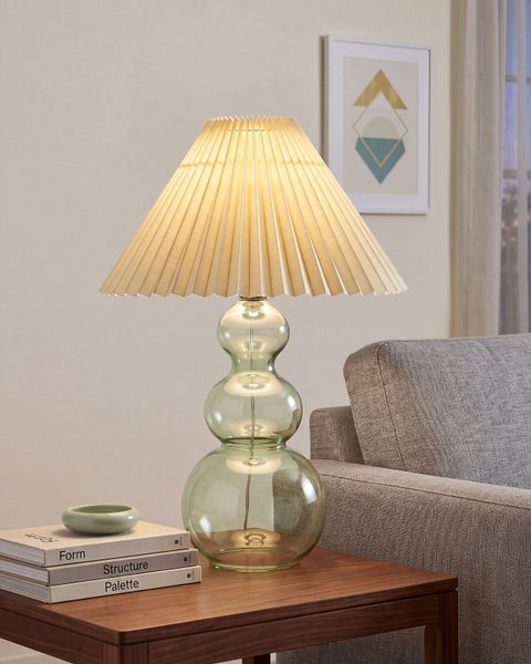 Tischlampe mit einem strukturierten Lampenschirm aus Stoff und einem transparenten Glasfuß in organischer Kugelform auf einem Beistelltisch.