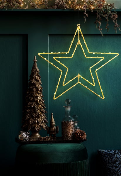 Festliche Dekoration mit beleuchtetem Stern, Zierbaum und dekorativen Flaschen auf einem Hocker