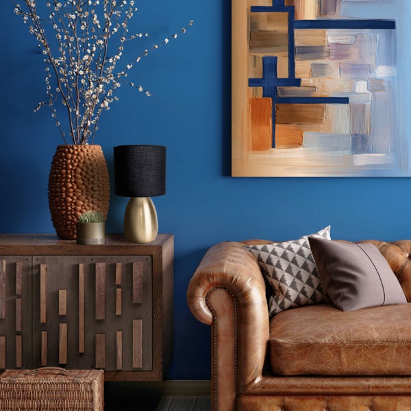 Wohnzimmer mit braunem Ledersofa, Kommode, Lampe, Dekoration und abstraktem Gemälde an einer blauen Wand