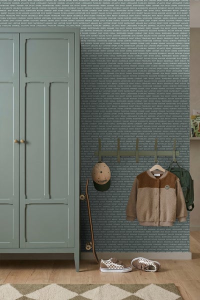 Kinderzimmer mit grünem Kleiderschrank, Motivtapete mit Text, Garderobe mit Pullover, Rucksack, Kappe und Sneakern, hell und organisiert gestaltet.