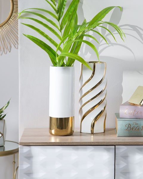Dekorative weiße Vasen mit goldenen Akzenten auf einem Sideboard.