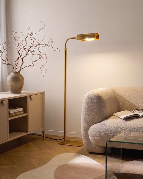 Moderne Stehlampe mit metallischem Design und verstellbarem Leuchtenkopf in einem gemütlichen Wohnzimmer mit Sofa und Kommode.