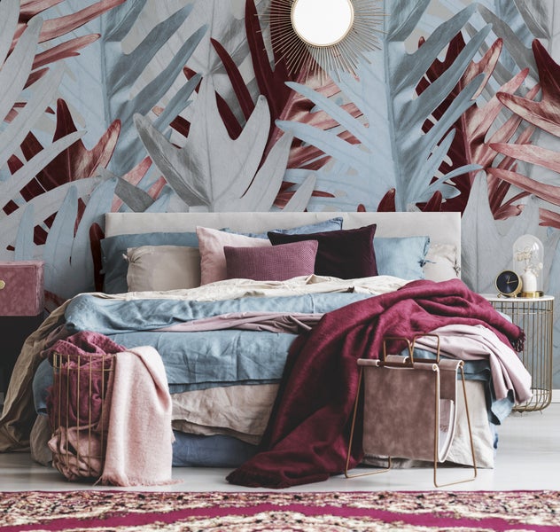 Schlafzimmer mit gemütlichem Bett und dekorativer Fototapete mit großen Blättern in Blau und Beerentönen sowie passender Dekoration.