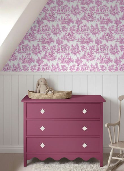 Kinderzimmer mit gemusterter Tapete, weißer Wandvertäfelung und einer rosa Kommode mit weißen Sterngriffen.