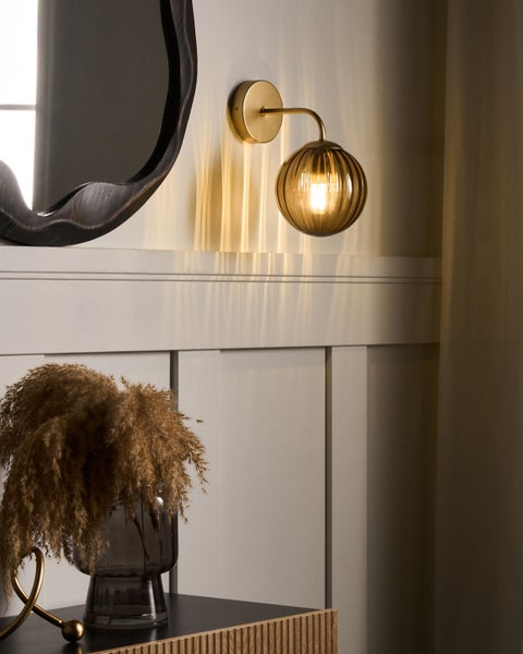 Wandleuchte aus Glas und Metall über einer Kommode mit Dekoration und einem Spiegel.