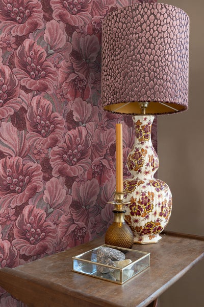 Dekorative Szene mit floraler Tapete, Tischlampe, Kerze und Dekorationsgegenständen auf einem Tisch