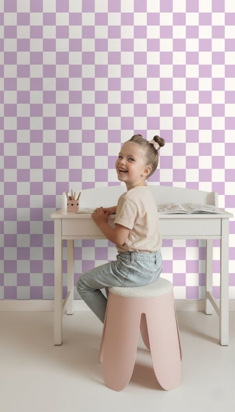 Mädchen sitzt an einem Schreibtisch vor einer Wand mit Schachbrettmuster.