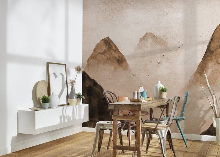 Fototapete mit einer Berglandschaft im Aquarell-Stil in einem hellen Esszimmer mit rustikalem Holztisch und verschiedenen Stühlen.