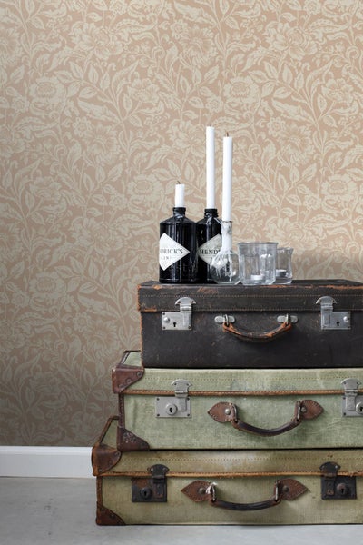 Vliestapete mit floralem Ornamentmuster im Vintage-Stil an einer Wand hinter drei gestapelten alten Koffern mit Dekoflaschen und Kerzen.