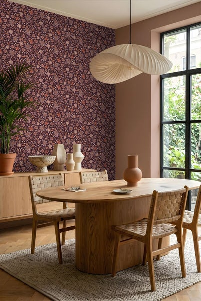 Vliestapete mit floralem Muster in einem hellen Esszimmer mit ovalem Holztisch, geflochtenen Stühlen und einem Sideboard.