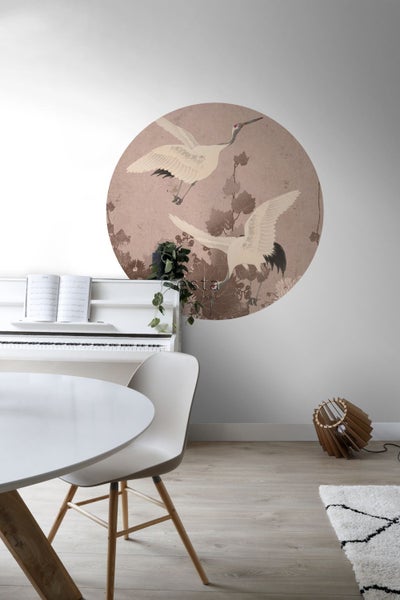 Wohnraum mit runder Wanddekoration, die Kraniche darstellt, sowie Klavier, Tisch und Lampe.