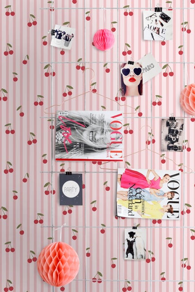 Dekoratives Wandgitter mit Fotos, Magazinen und Papierdekorationen vor einer gestreiften Kirschtapete.