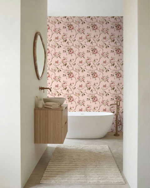 Badezimmer mit einer Vliestapete mit Rosenmuster an der Wand hinter einer freistehenden Badewanne, kombiniert mit einem Waschtisch aus Holz.