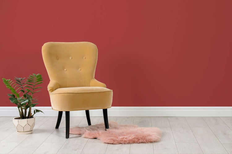 Modern gestalteter Raum mit rot gestrichener Wand, gelbem Samtsessel, Zimmerpflanze und rosa Fellteppich auf hellem Laminatboden.