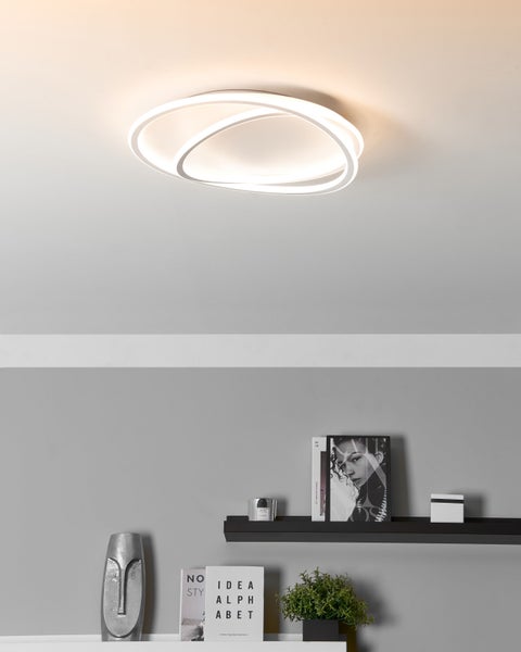 Moderne LED-Deckenleuchte mit drei ineinandergreifenden weißen Ringen in einem hellen Raum mit Wandregal und Dekoration.