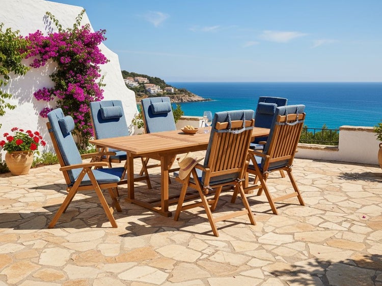 Gartenmöbel-Set aus Holz mit rechteckigem Tisch und sechs Klappstühlen mit blauen Auflagen auf einer Steinterrasse mit Meerblick.