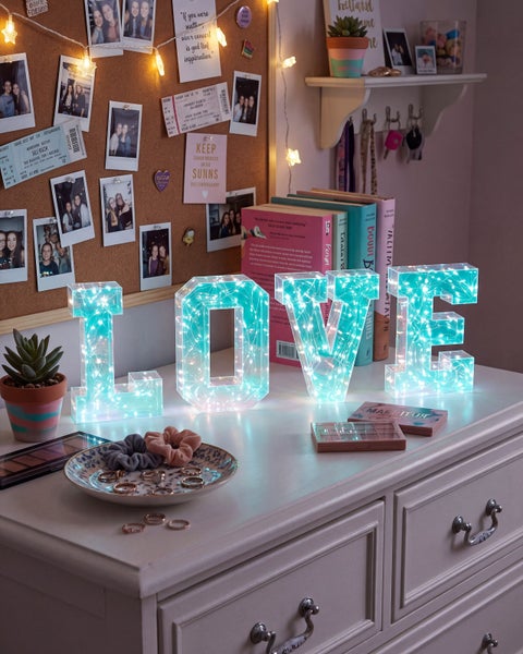 Dekorative LOVE Leuchtbuchstaben aus Acryl mit LED Draht Lichterkette auf einer Kommode in einem liebevoll dekorierten Zimmer.