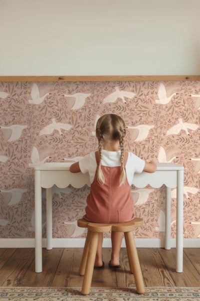 Mädchen sitzt an einem Schreibtisch vor einer Tapete mit Schwanmuster