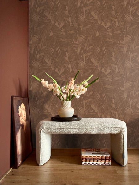 Wohnraum mit gemusterter Vliestapete mit Blattmotiv, kombiniert mit unifarbener Wand, Polsterbank, Blumenvase und gerahmtem Wandbild.