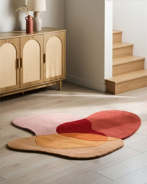 Abstrakter Teppich mit organischen Formen auf hellem Holzboden neben einem Sideboard aus Holz und einer Treppe in einem hellen Raum.