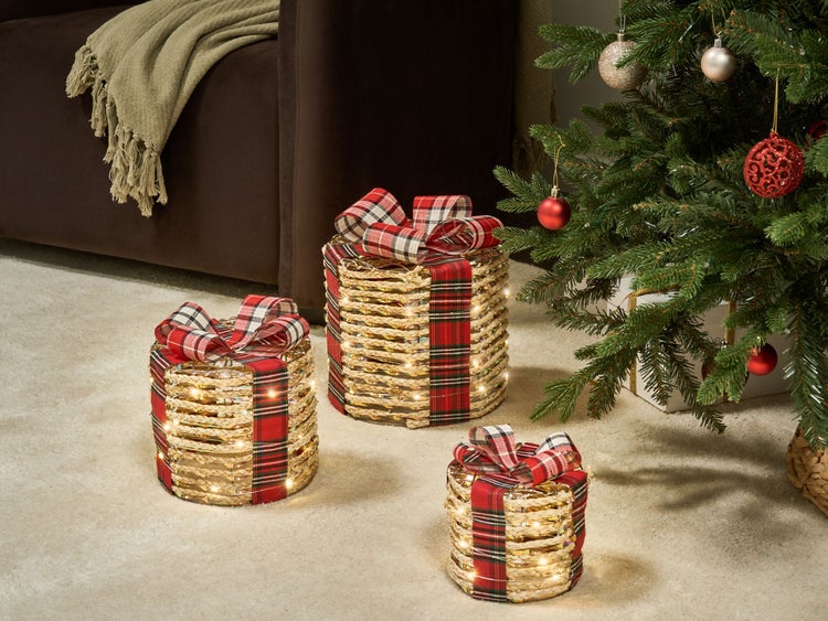 Dekorative geflochtene Geschenke mit Karoband und Beleuchtung unter einem Weihnachtsbaum.