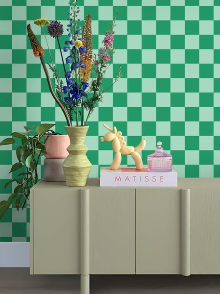 Vliestapete mit Karomuster hinter einer Kommode mit Blumen und Dekoration in einem modern eingerichteten Raum.
