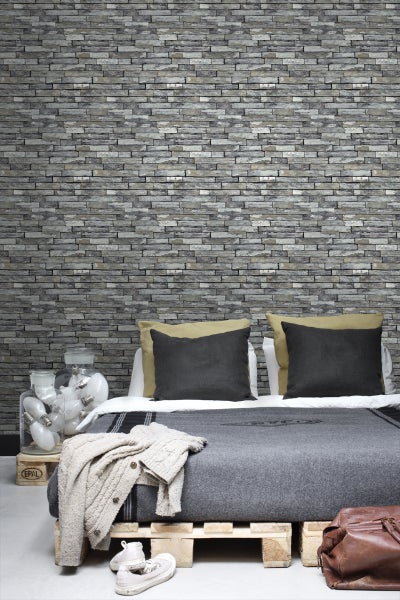 Wohnraum mit Wandverkleidung in Steinoptik, Bett auf Europaletten und dekorativen Elementen