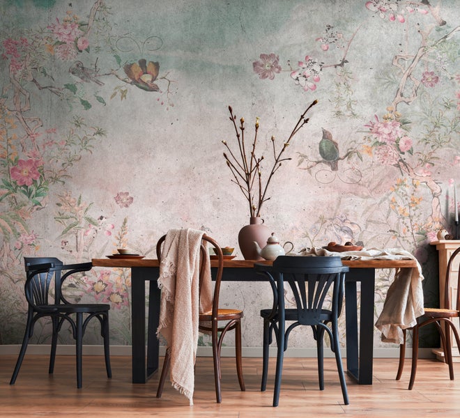 Esszimmer mit floraler Wandtapete im Vintage-Stil, Holztisch, schwarzen und braunen Stühlen sowie Tischdekoration auf Parkettboden.